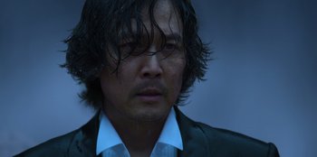 Movie still from “Squid Game” (2021), created by Hwang Dong-hyuk – A person wearing a suit and tie; Close Up shot, Low angle