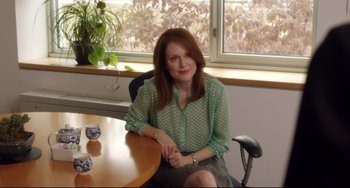 Movie still from “Still Alice” (2014), directed by Richard Glatzer – A woman sitting at a wooden table in front of a window; Medium shot, Over the shoulder angle