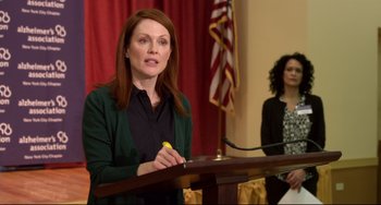 Movie still from “Still Alice” (2014), directed by Richard Glatzer – Julianne moore speaking at a podium in front of a microphone; Medium shot, Over the shoulder angle