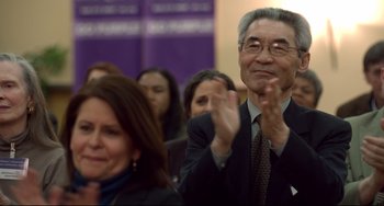 Movie still from “Still Alice” (2014), directed by Richard Glatzer – An older man clapping in front of a group of people; Close Up shot, Over the shoulder angle