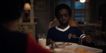 Movie still from “Stranger Things” (2016), created by Ross Duffer – A boy sitting at a dinner table with a plate of food in front of him; Close Up shot, Over the shoulder angle