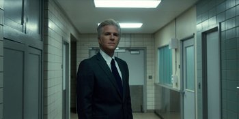 Movie still from “Stranger Things” (2016), created by Ross Duffer – A man in a suit and tie standing in a hallway; Medium shot, Low angle