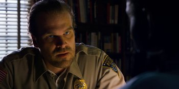 Movie still from “Stranger Things” (2016), created by Ross Duffer – A man in a police uniform looking at a computer screen; Close Up shot, Over the shoulder angle