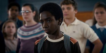 Movie still from “Stranger Things” (2016), created by Ross Duffer – A young man standing in front of a group of people; Close Up shot, Over the shoulder angle