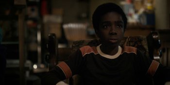 Movie still from “Stranger Things” (2016), created by Ross Duffer – A young boy sitting in a chair looking at the camera; Close Up shot, High angle