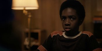 Movie still from “Stranger Things” (2016), created by Ross Duffer – A young man sitting in front of a lamp in a living room; Close Up shot, Over the shoulder angle