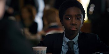 Movie still from “Stranger Things” (2016), created by Ross Duffer – A boy in a suit and tie holding a cup of coffee; Close Up shot, Over the shoulder angle