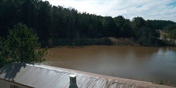 Movie still from “Stranger Things” (2016), created by Ross Duffer – A body of water surrounded by trees and a wooden deck; Extreme Wide shot, High angle