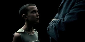 Movie still from “Stranger Things” (2016), created by Ross Duffer – A young boy is looking up at an older man; Medium shot, Over the shoulder angle