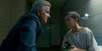 Movie still from “Stranger Things” (2016), created by Ross Duffer – A man and a boy in a hospital room talking to each other; Medium shot, Over the shoulder angle