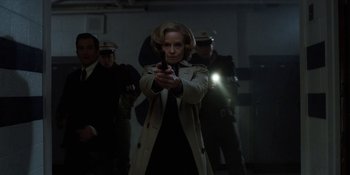 Movie still from “Stranger Things” (2016), created by Ross Duffer – A woman in a trench coat is holding a gun; Medium shot, Low angle