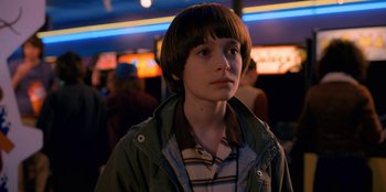 Movie still from “Stranger Things” (2016), created by Ross Duffer – A boy with a brown hair and a brown shirt is looking to his left; Close Up shot, Over the shoulder angle
