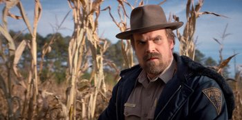 Movie still from “Stranger Things” (2016), created by Ross Duffer – A man with a beard wearing a hat and a jacket; Medium shot, Over the shoulder angle
