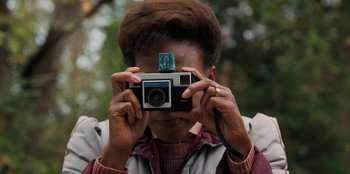 Movie still from “Stranger Things” (2016), created by Ross Duffer – A woman taking a picture with an old camera; Close Up shot, Low angle