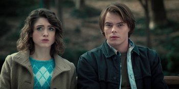 Movie still from “Stranger Things” (2016), created by Ross Duffer – A man and a woman sitting next to each other in front of trees; Close Up shot, Over the shoulder angle