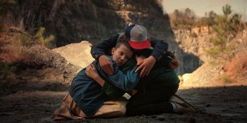 Movie still from “Stranger Things” (2016), created by Ross Duffer – A couple of people that are sitting on the ground together; Medium shot, High angle