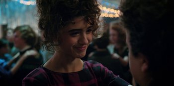 Movie still from “Stranger Things” (2016), created by Ross Duffer – A person with curly hair smiling; Close Up shot, Over the shoulder angle
