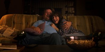 Movie still from “Stranger Things” (2016), created by Ross Duffer – A man and a woman sitting on a couch hugging; Medium shot, Low angle