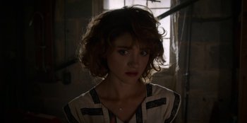 Movie still from “Stranger Things” (2016), created by Ross Duffer – A young woman with curly brown hair wearing a white shirt; Close Up shot, Over the shoulder angle