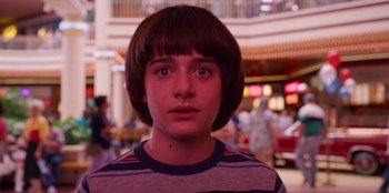 Movie still from “Stranger Things” (2016), created by Ross Duffer – A young boy with brown hair stares into the camera; Close Up shot, Over the shoulder angle