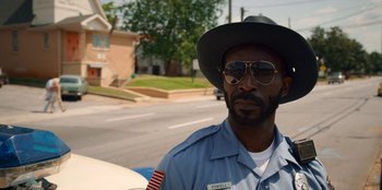 Movie still from “Stranger Things” (2016), created by Ross Duffer – A man in a hat and sunglasses standing on the side of the road; Close Up shot, Over the shoulder angle