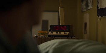 Movie still from “Stranger Things” (2016), created by Ross Duffer – An alarm clock sitting on top of a nightstand next to a bed; Extreme Close Up shot, Low angle