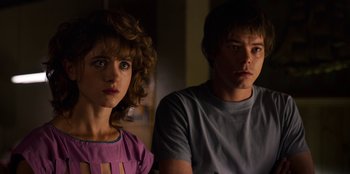 Movie still from “Stranger Things” (2016), created by Ross Duffer – A man and a woman sitting next to each other in a room; Close Up shot, Over the shoulder angle
