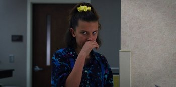 Movie still from “Stranger Things” (2016), created by Ross Duffer – A woman with a yellow bow in her hair looking into a mirror; Close Up shot, Over the shoulder angle
