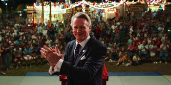Movie still from “Stranger Things” (2016), created by Ross Duffer – A man in a suit clapping in front of a crowd; Medium shot, Over the shoulder angle