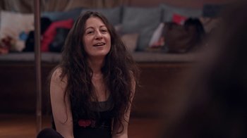 Movie still from “Strip Down, Rise Up” (2021), directed by Michèle Ohayon – A woman sitting on a couch with her eyes closed; Medium shot, Over the shoulder angle