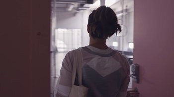 Movie still from “Strip Down, Rise Up” (2021), directed by Michèle Ohayon – A woman with a purse walking down a hall way; Medium shot, Over the shoulder angle