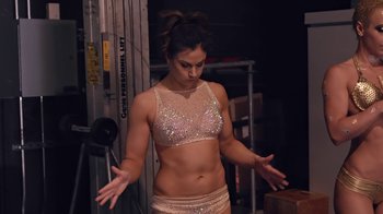 Movie still from “Strip Down, Rise Up” (2021), directed by Michèle Ohayon – A woman in a bra and shorts standing in front of a wall; Medium shot, Low angle