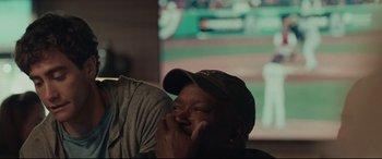 Movie still from “Stronger” (2017), directed by David Gordon Green – A man in a baseball cap is sitting in front of a television; Close Up shot, Over the shoulder angle