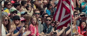 Movie still from “Stronger” (2017), directed by David Gordon Green – A group of people sitting in front of an american flag; Medium shot, Over the shoulder angle