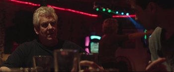 Movie still from “Stronger” (2017), directed by David Gordon Green – A man sitting at a table in front of a neon sign; Close Up shot, Over the shoulder angle