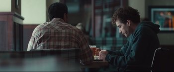 Movie still from “Stronger” (2017), directed by David Gordon Green – A man sitting at a table with a glass of beer in front of another man; Medium shot, Over the shoulder angle