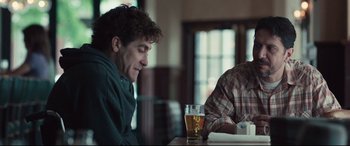 Movie still from “Stronger” (2017), directed by David Gordon Green – A man sitting at a table with a glass of beer in front of him; Medium shot, Over the shoulder angle