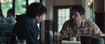 Movie still from “Stronger” (2017), directed by David Gordon Green – Two men sitting at a table with a glass of beer in front of them; Medium shot, Over the shoulder angle