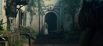 Movie still from “Sweet Tooth” (2021), created by Jim Mickle – A man sitting on a bench in front of an arched doorway; Wide shot, Low angle