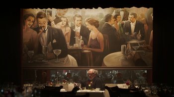 Movie still from “Mr. Robot” (2015), created by Sam Esmail – A man sitting at a table in front of a painting; Wide shot, Over the shoulder angle