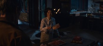 Movie still from “Sweet Tooth” (2021), created by Jim Mickle – A woman holding a knife in front of a wooden table; Medium shot, Over the shoulder angle