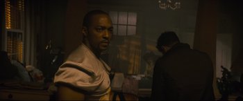 Movie still from “Synchronic” (2019), directed by Justin Benson – A man standing next to another man in a dark room; Medium shot, Over the shoulder angle