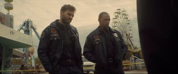 Movie still from “Synchronic” (2019), directed by Justin Benson – Two police officers standing next to each other near a ferris wheel; Medium shot, Over the shoulder angle