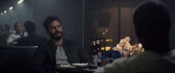 Movie still from “Synchronic” (2019), directed by Justin Benson – A man sitting at a table with a bottle of beer in front of him; Medium shot, Over the shoulder angle