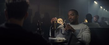 Movie still from “Synchronic” (2019), directed by Justin Benson – A man sitting at a table with a bottle of beer; Medium shot, Low angle