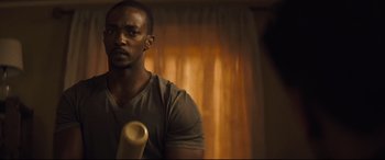 Movie still from “Synchronic” (2019), directed by Justin Benson – A man holding a baseball bat in a room; Close Up shot, Over the shoulder angle