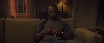 Movie still from “Synchronic” (2019), directed by Justin Benson – A man sitting on a couch with a bottle in front of him; Medium shot, High angle