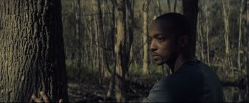 Movie still from “Synchronic” (2019), directed by Justin Benson – A man standing next to a tree in the woods; Close Up shot, Over the shoulder angle