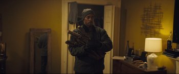 Movie still from “Synchronic” (2019), directed by Justin Benson – A man holding a bunch of wood in a room; Medium shot, Over the shoulder angle