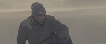 Movie still from “Synchronic” (2019), directed by Justin Benson – A man in a winter coat and a hat is sitting in the snow; Medium shot, Low angle